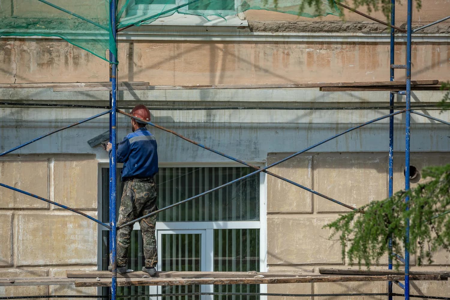 Fassadendämmung an einem Wohnhaus: Handwerker verputzt die Fassade vom Gerüst aus